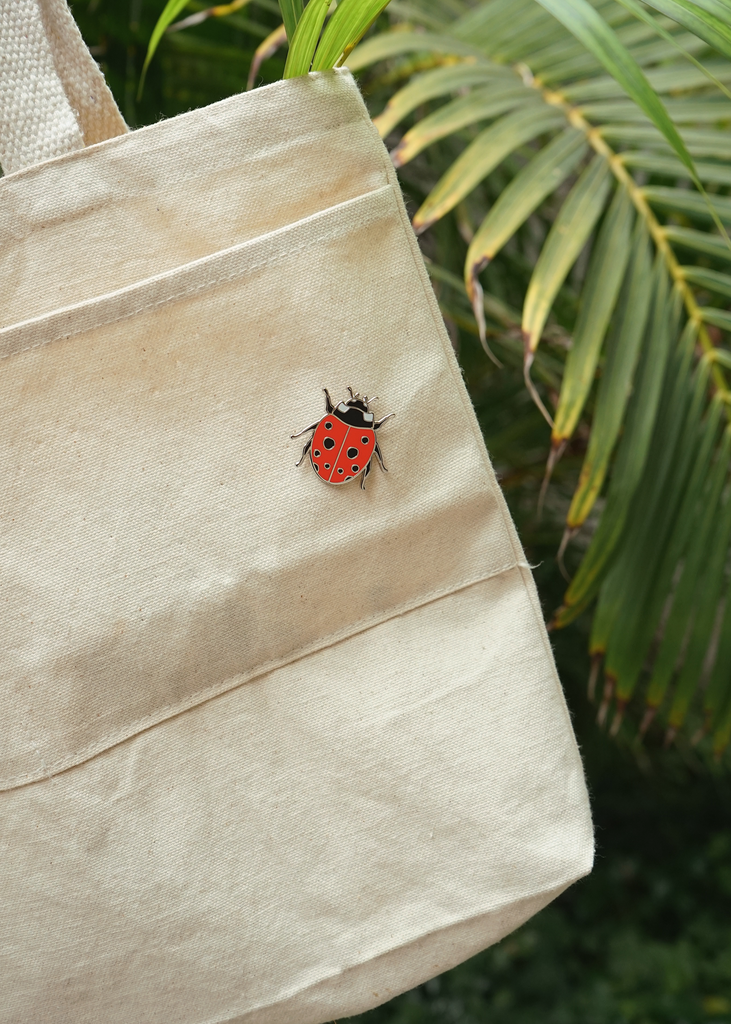 Cherry red enamel ladybug pin on canvas tote bag