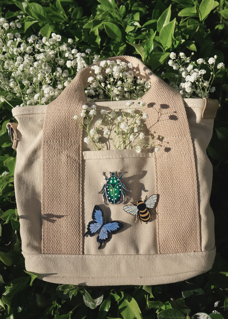Green spotted rose chafer beetle pin on bag next to honeybee and blue swallowtail pin
