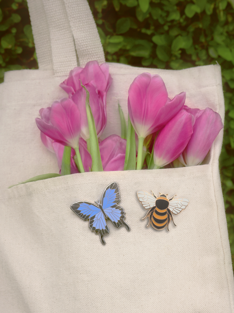 Blue swallowtail and honeybee pins on canvas tote bag with pink tulips in pocket of bag