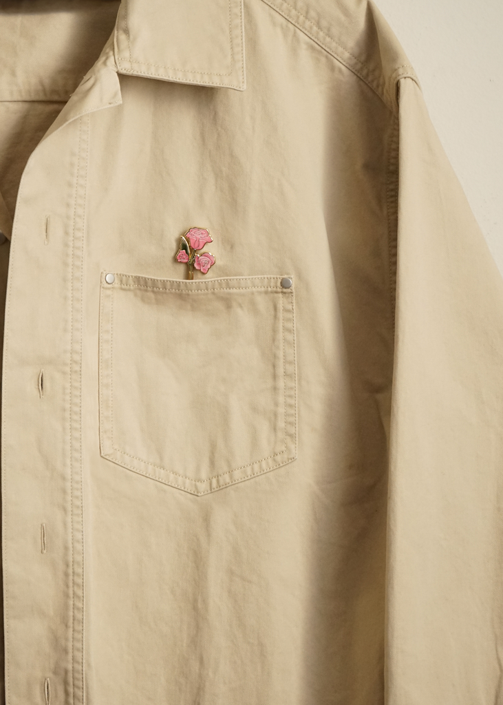 Beige jacket with a pink rose pin on the chest pocket against a beige background