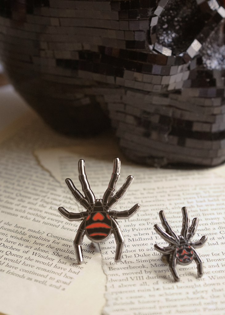 Black widow spider mini pin and black widow regular size Carnal Flora pins on page of book