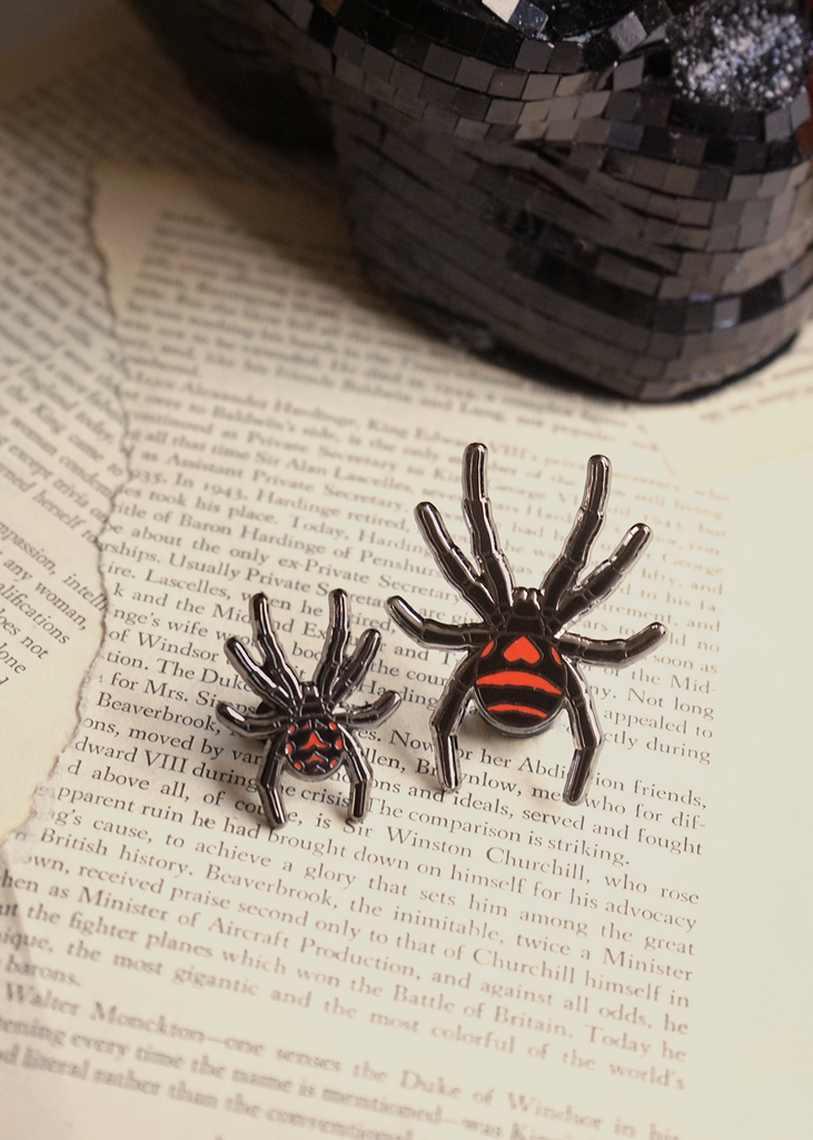 Black widow spider mini pin and black widow regular size pins on page of book