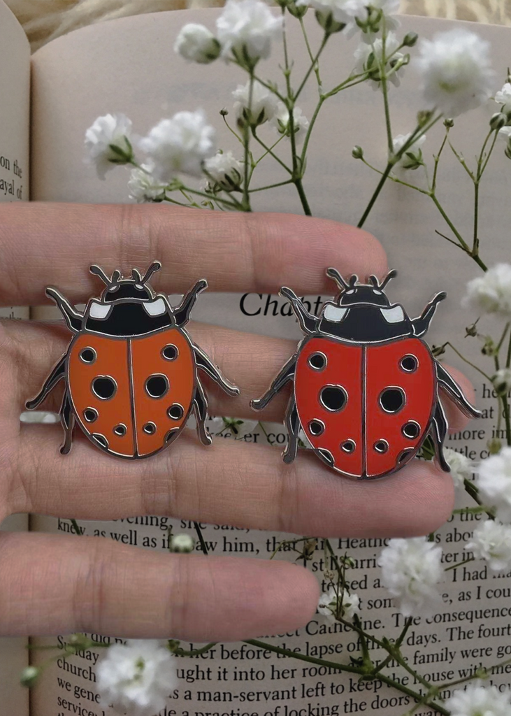 Cherry red and tomato red enamel ladybug pins on hand