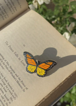 Video of orange monarch enamel pin on book