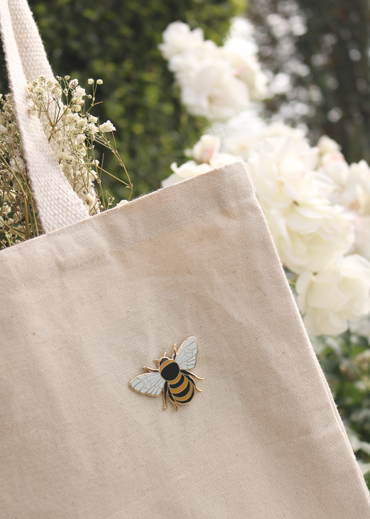 Close up of honey bee pin on tote bag in front of rose bush